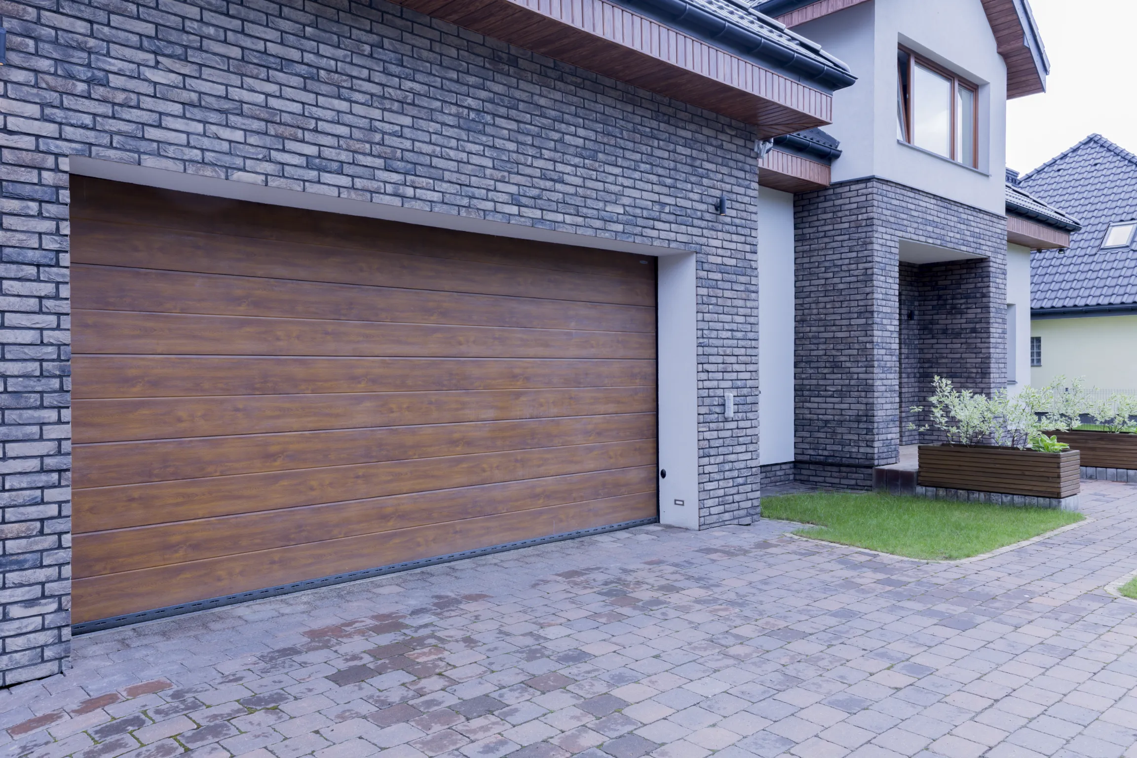 Modern brick home featuring a wooden garage door installation.